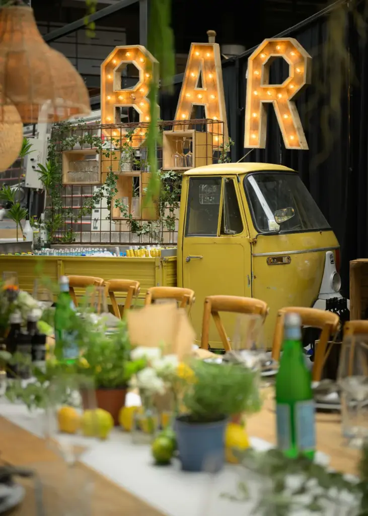 Verlichte BAR-letters boven een gele Piaggio Ape als bar op het bedrijfsfeest van Brouwers Reklame