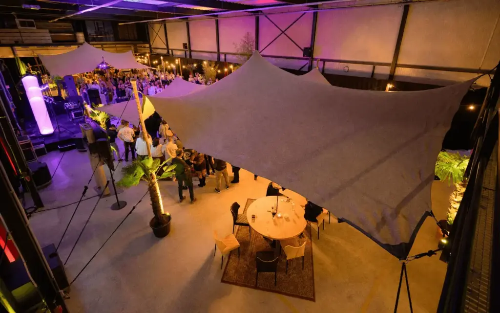 Overzicht van de feestzaal tijdens het bedrijfsfeest van Brouwers Reklame, met stretchtenten, palmen en een podium